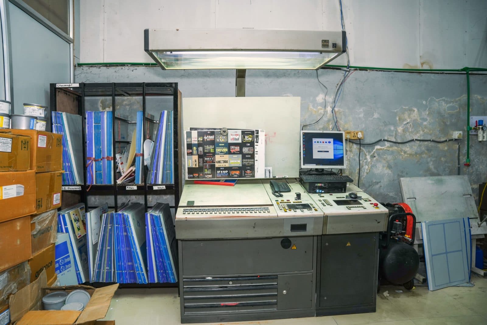 Prepress: offset plates racked beside the plate-setter console under a colour-viewing lamp
